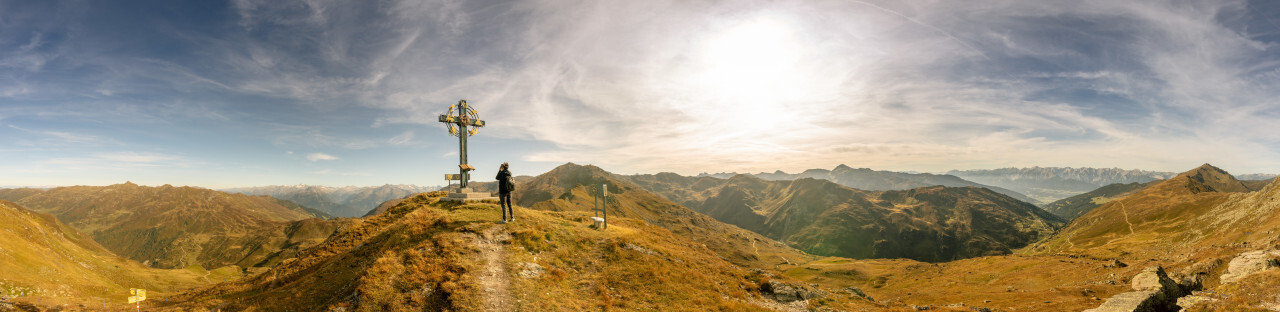 Landscape panorama of the Austrian Alps Hiker stands at the summit cross