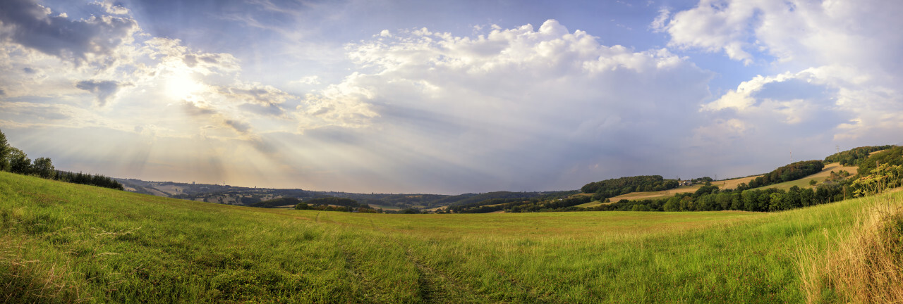 Sun rays break through the clouds over a rural landscape with fields in Germany near Velbert Langenberg, Neviges in North Rhine Westphalia