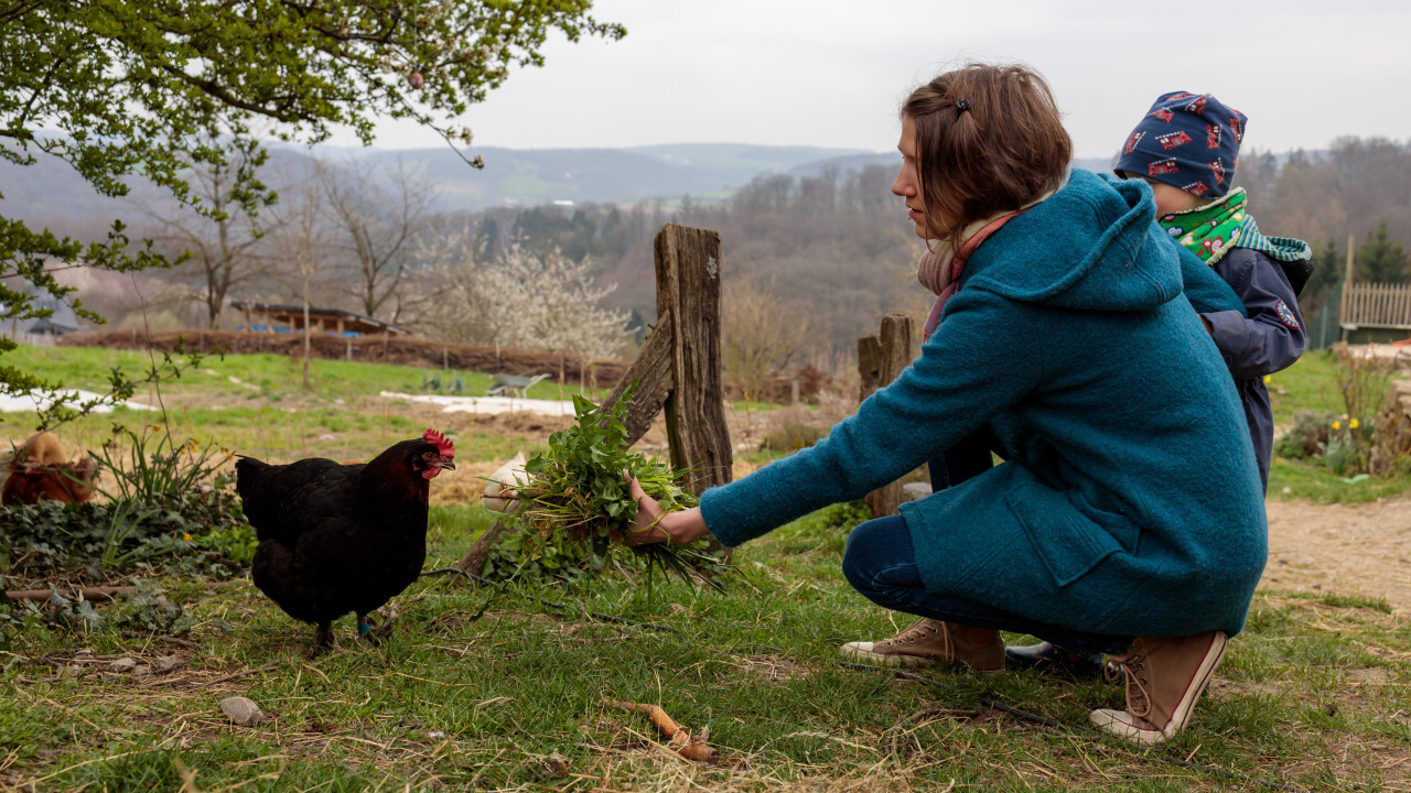 Young woman in blue coat feeds a black hen