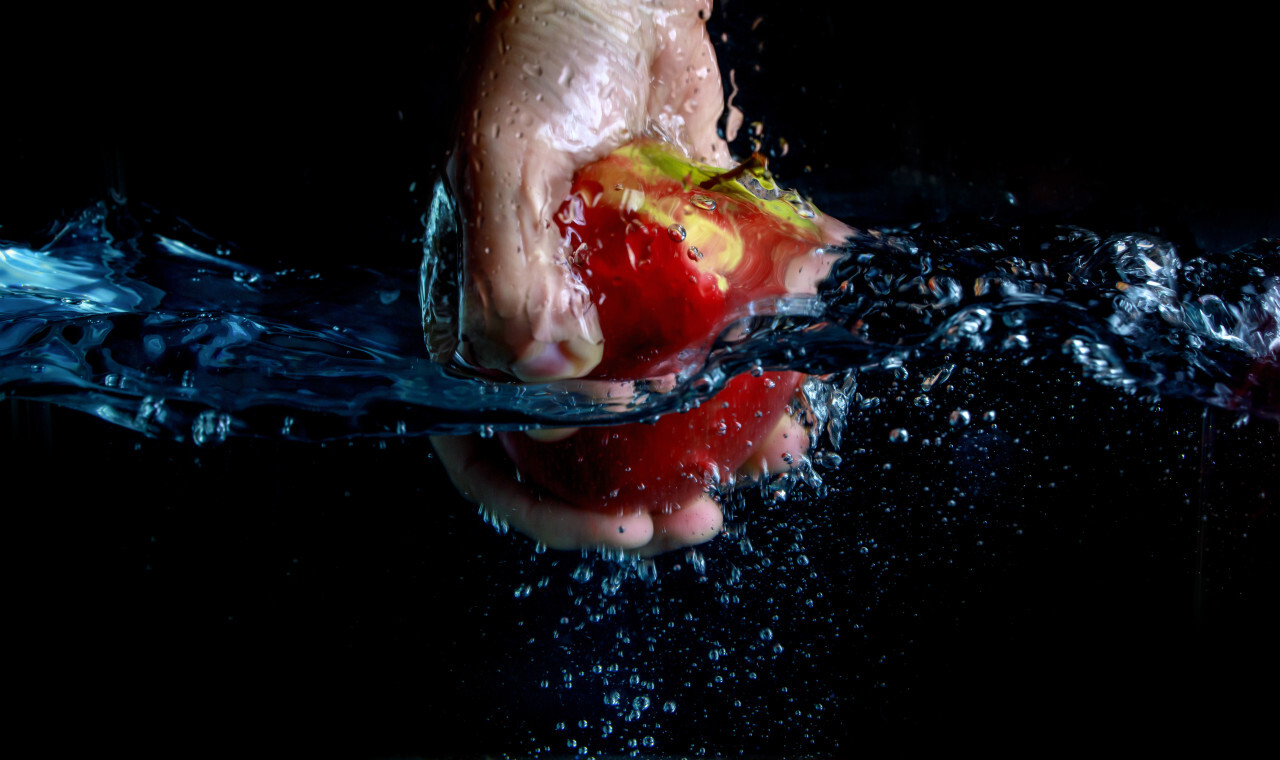 An apple being pulled out of the water by hand isolated on a black background