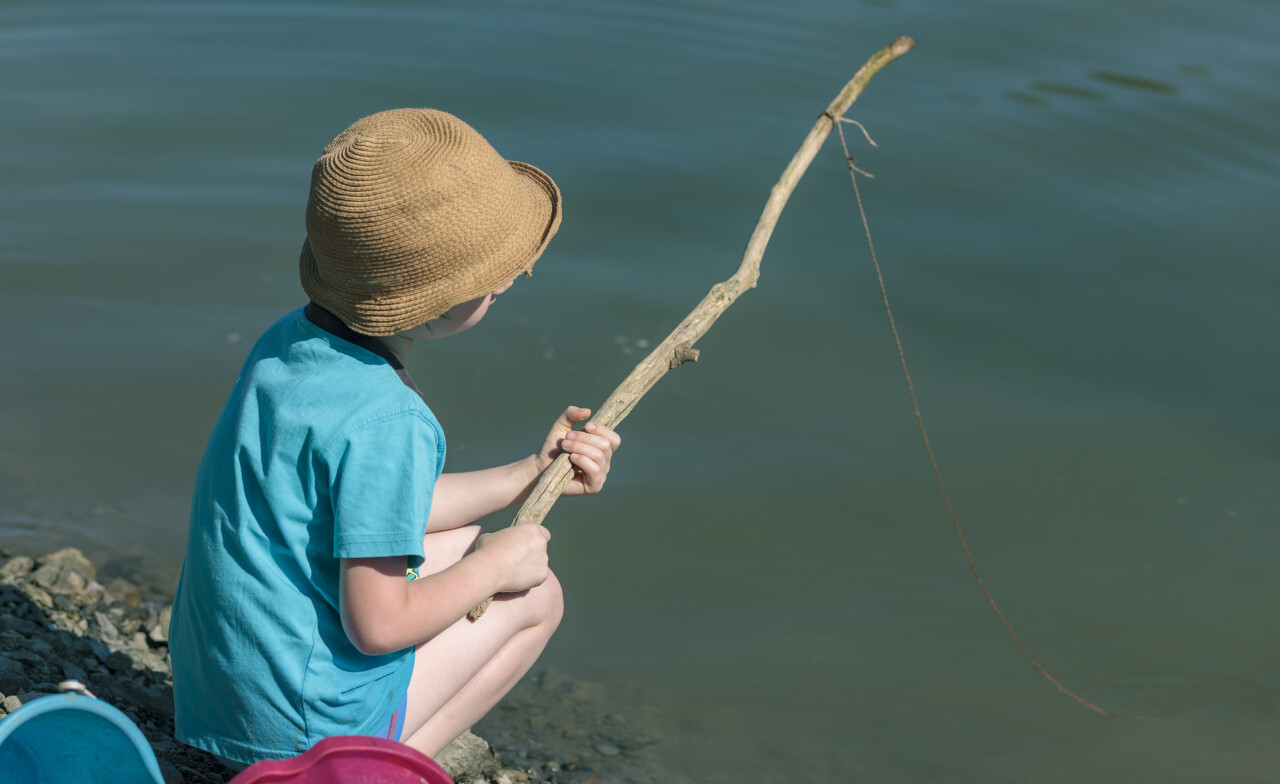 child with a self-made fishing rod from a branch and a line on a lake