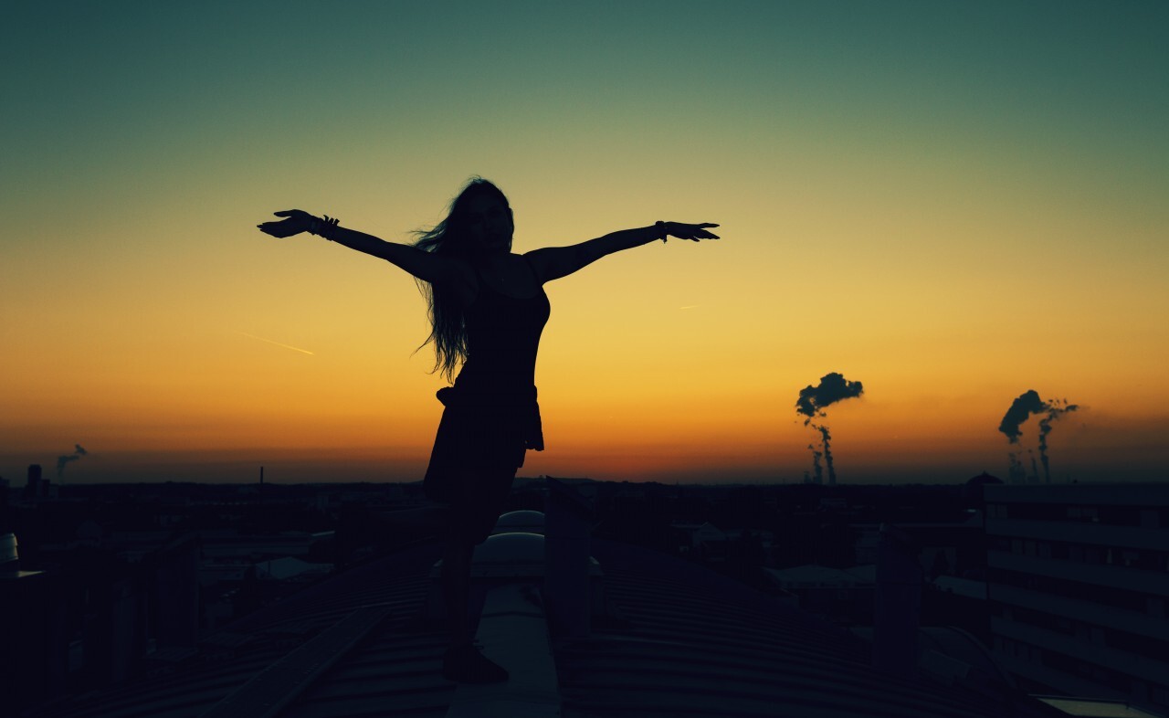 A girl on the roofs of a city holds out her arms and enjoys the sunset