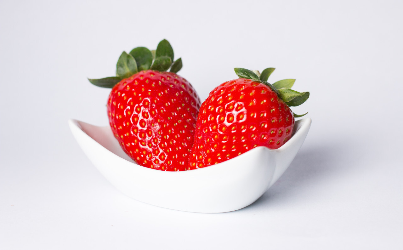 Red ripe strawberry in the white bowl, light background