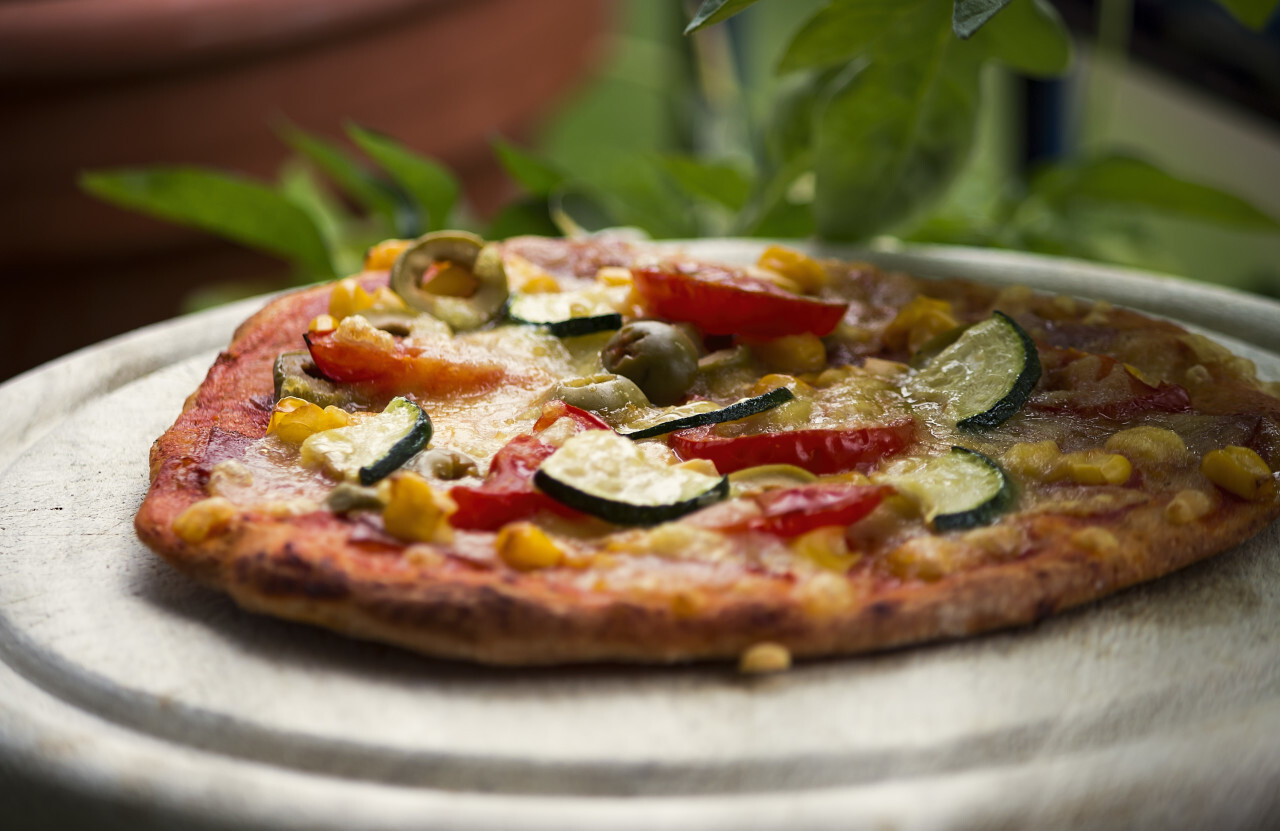 pizza with zucchini spinach olives corn tomatoes on a wooden board