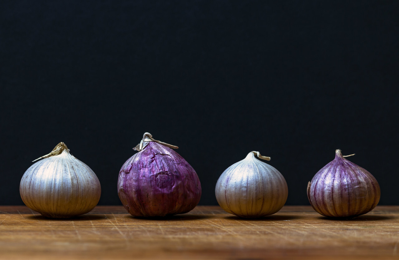 four garlic bulbs on a wooden board - black background