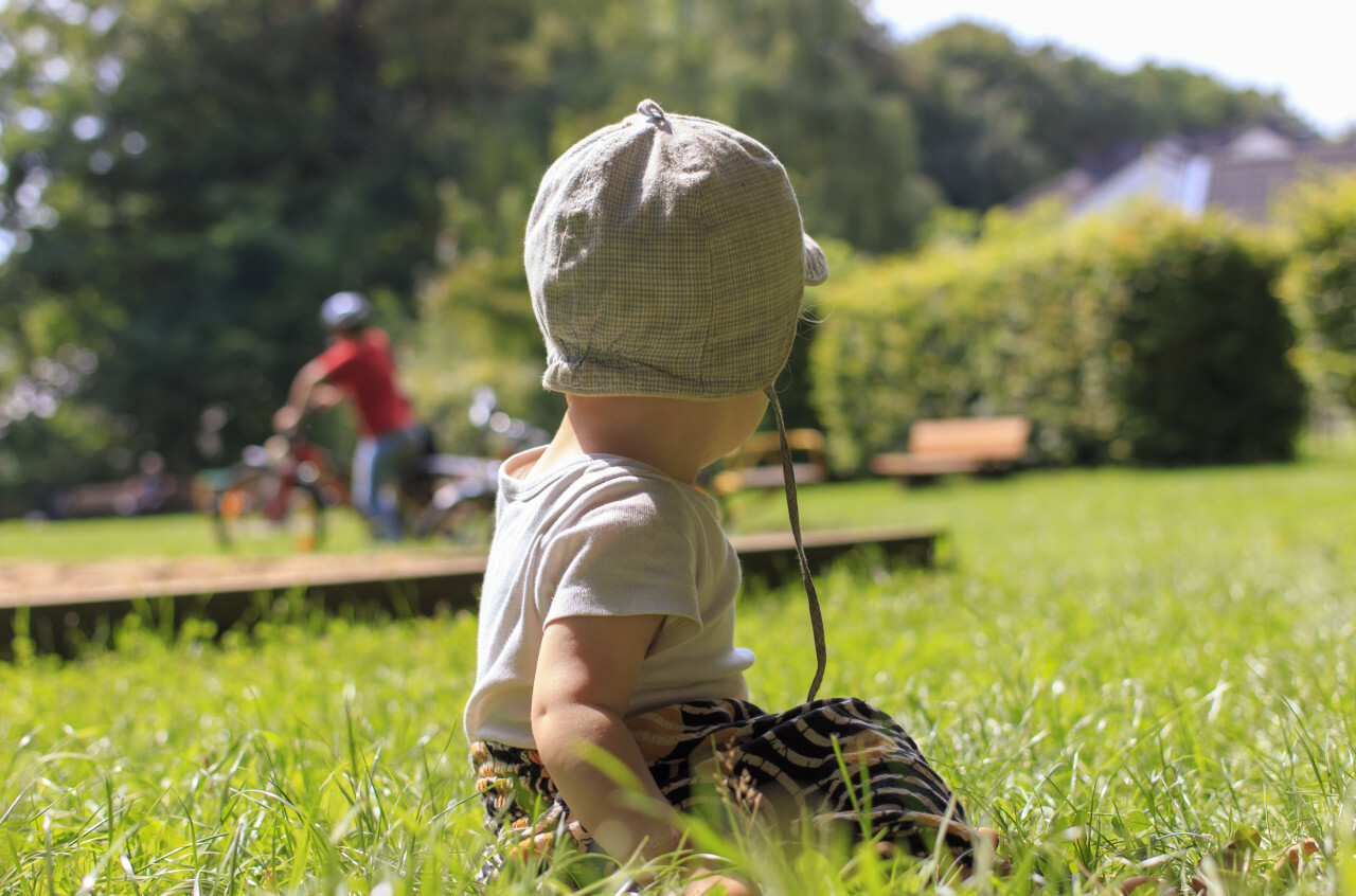 Baby watches the big children curiously while playing on a playground