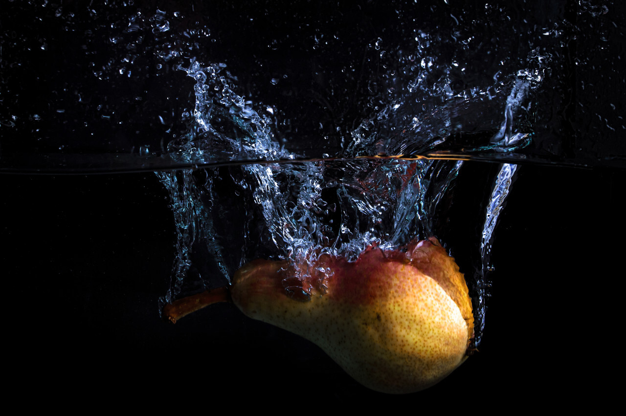 Pear falls into the water with lots of water splashes on a black background