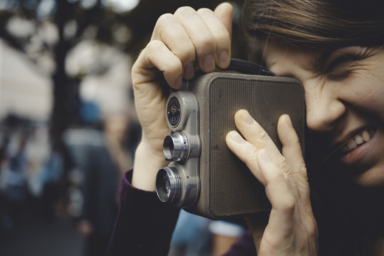 young woman is filming with an old movie camera