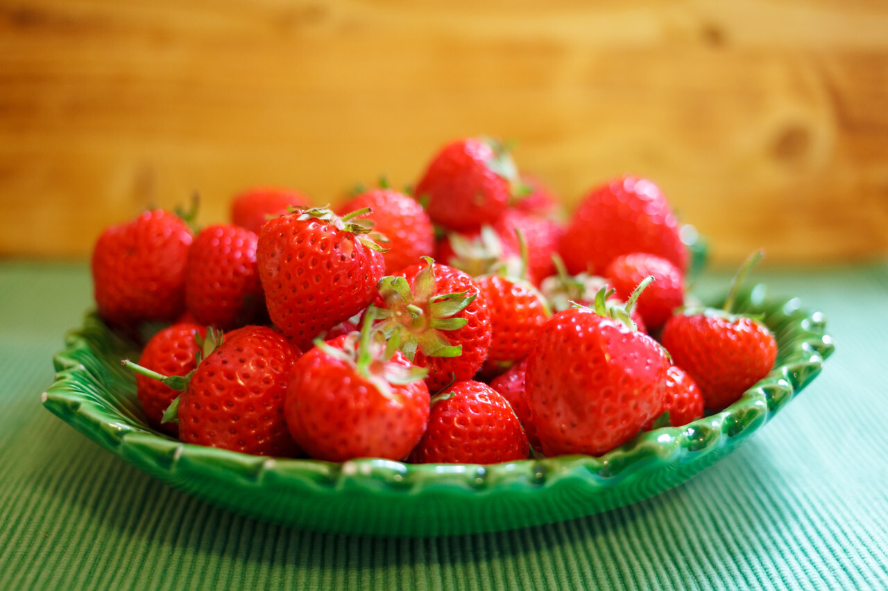 fresh red strawberries in a green bowl on wooden background