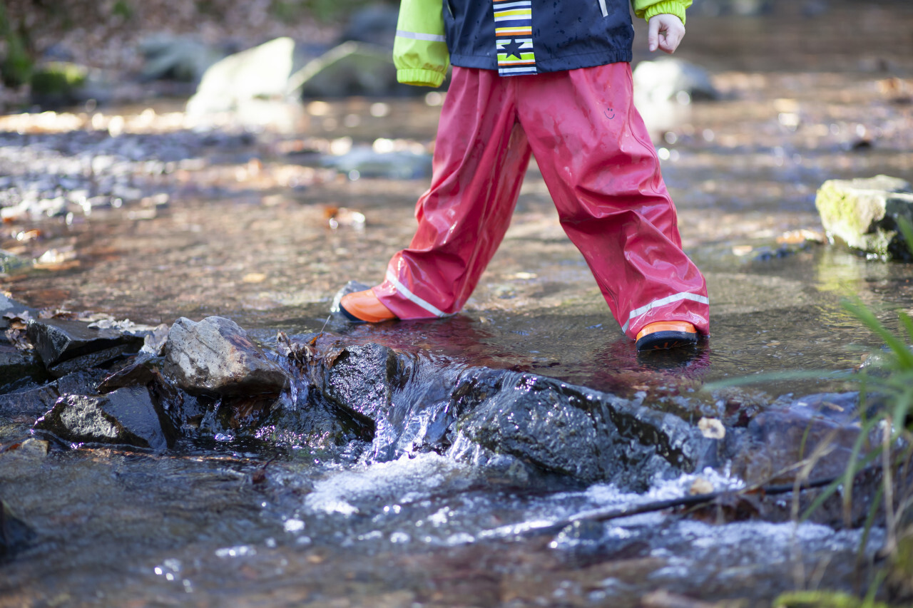 Child with rainwear and rubber boots standing in a stream