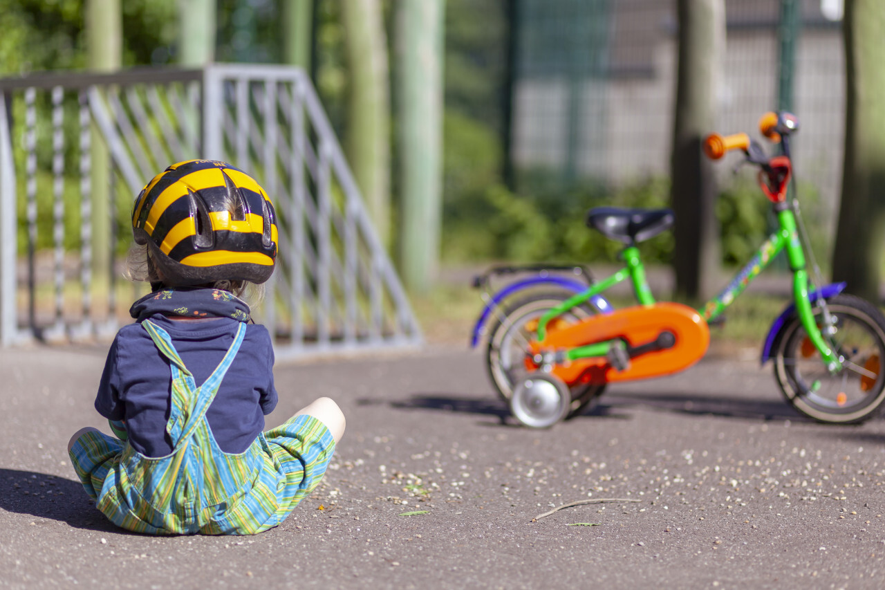 Child sits on the floor of a playground in front of his bike