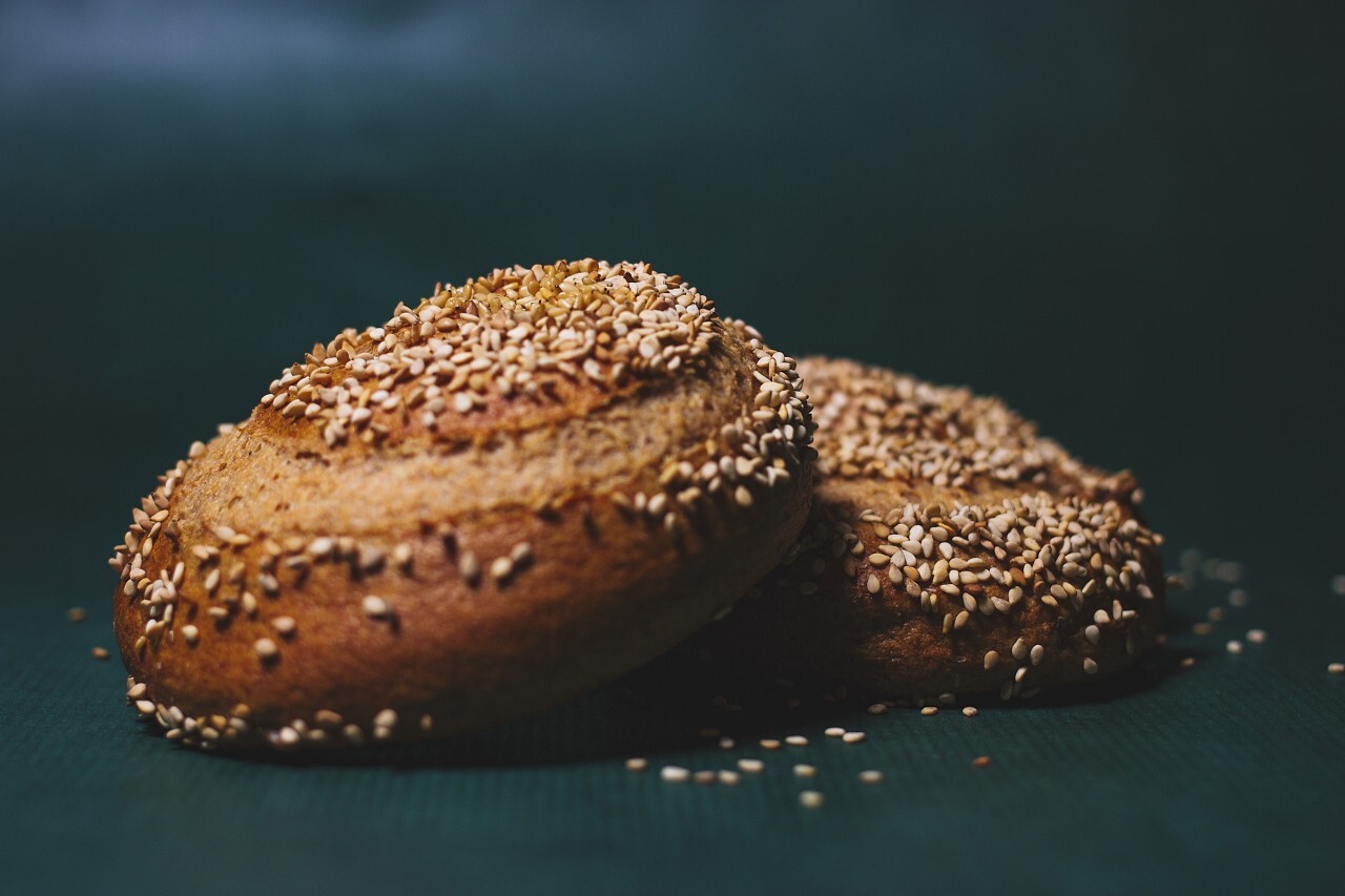 homemade burger rolls sprinkled with sesame seeds on a green background