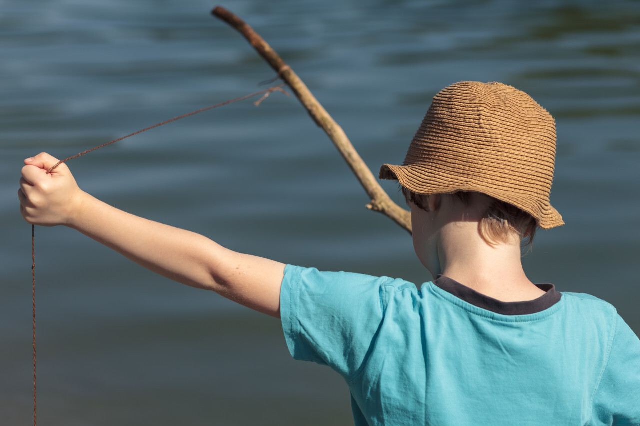 child with a self-made fishing rod from a branch and a line on a lake