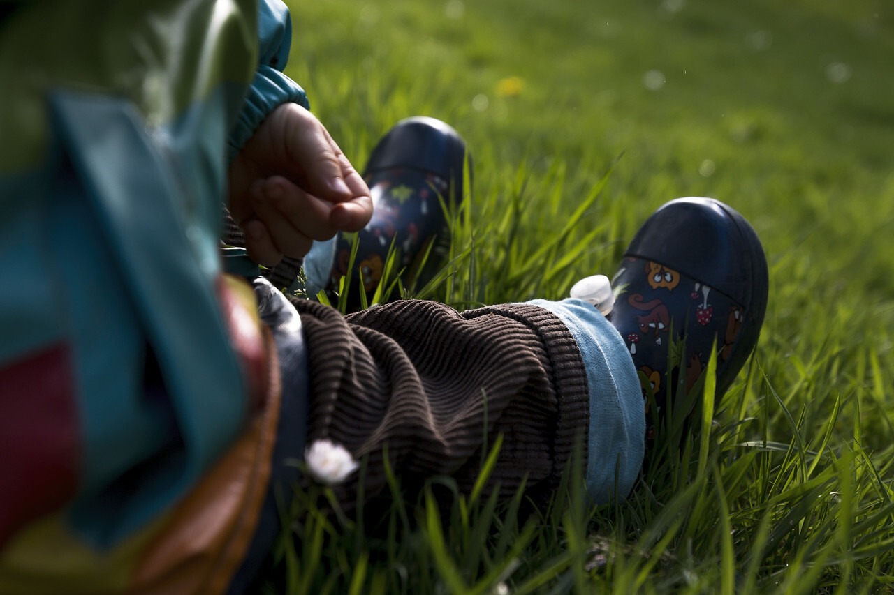 child in rubber boots sits on meadow