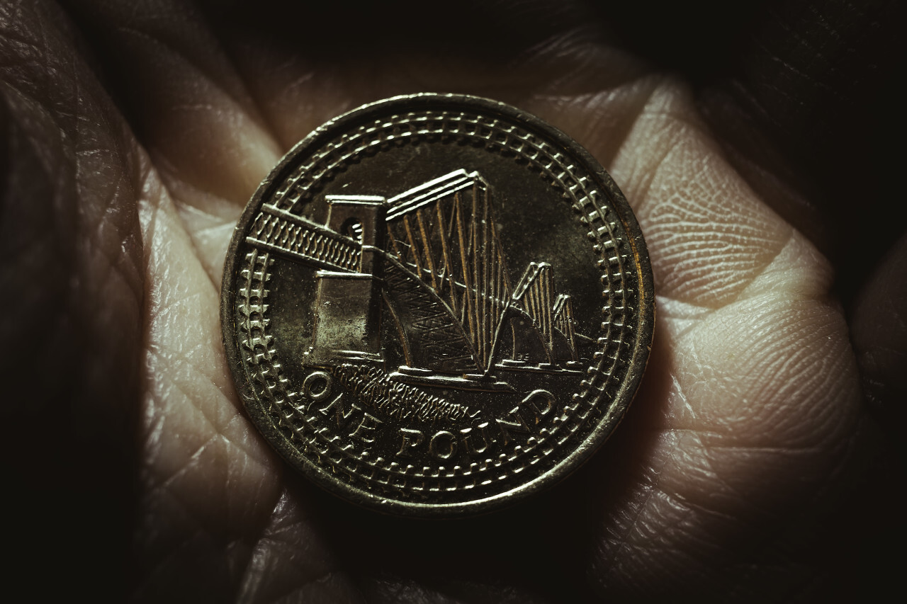 One British pound in a hand, money coin background