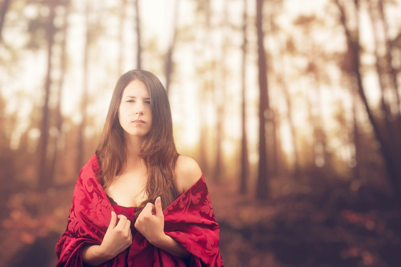 Beautiful girl in a chic red dress posing in the fairy autumn forest