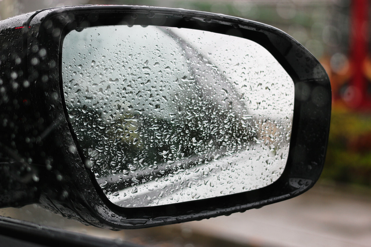 Closeup of car side rear view mirror with rain drops