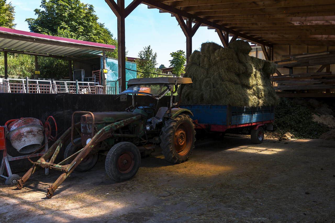 old green tractor with hay loaded trailer