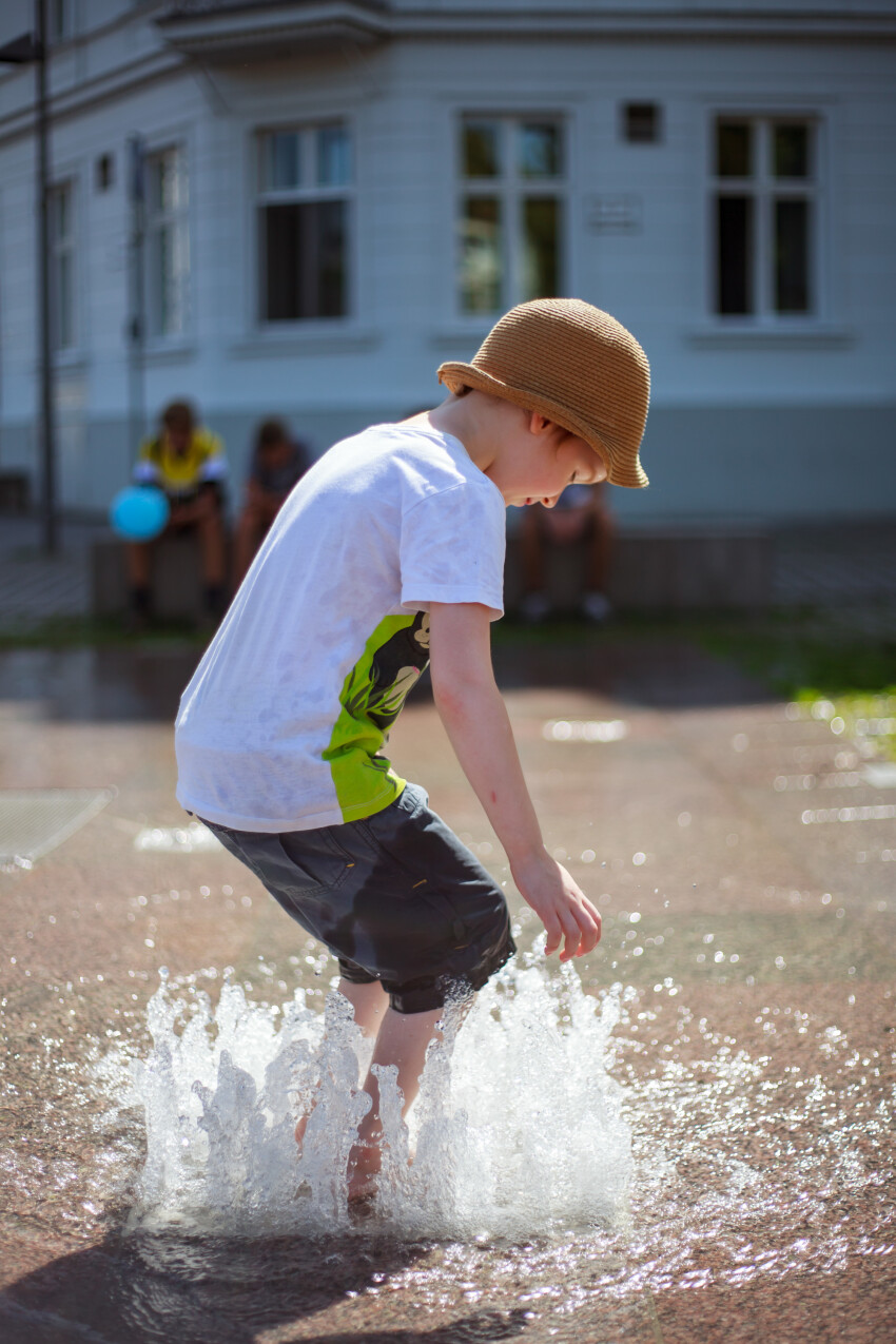 Child plays with the water from a fountain in summer