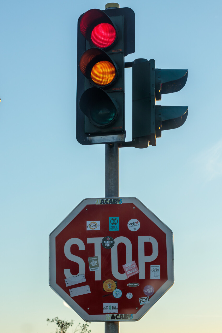 Stop sign full of stickers below a traffic light