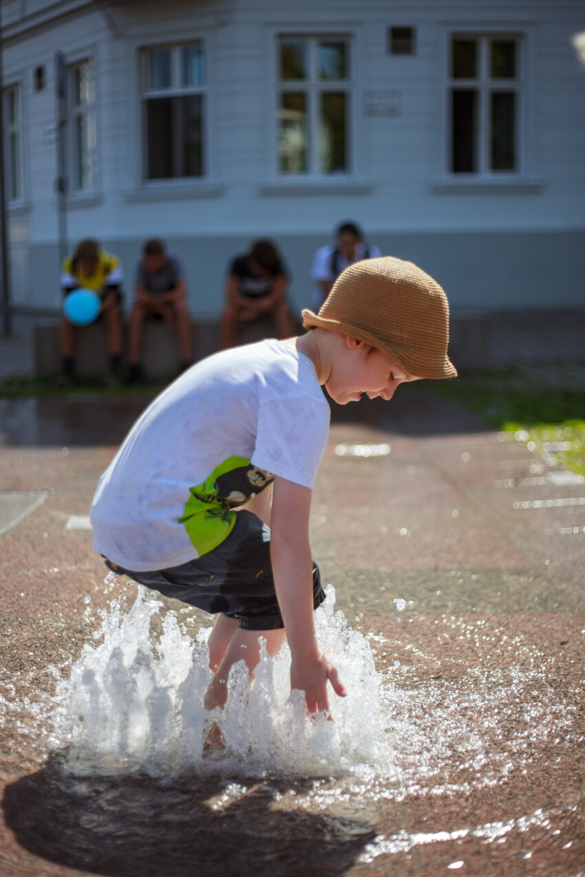 Little Boy plays with the water from a fountain in summer