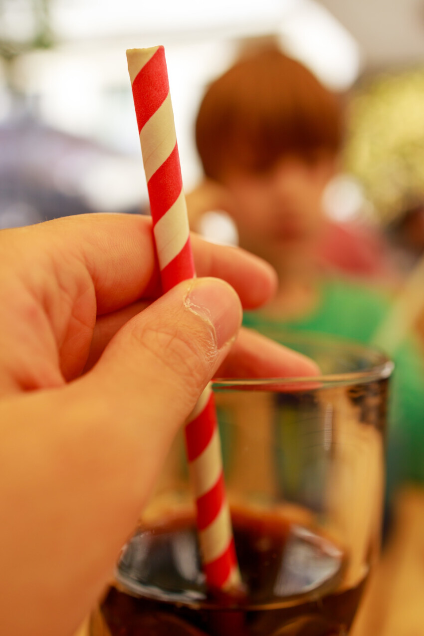 A glass of cola with one hand on the straw