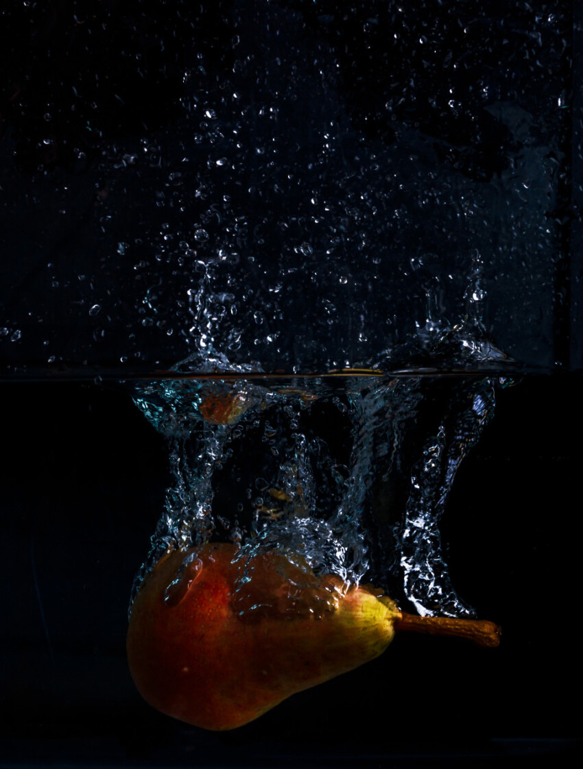 Pear falls into the water with lots of water splashes on a black background