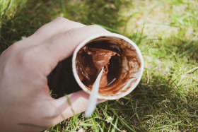 Stock Image: A mug of chocolate ice cream in hand over a meadow in summer