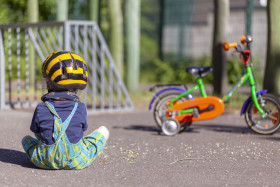 Stock Image: Child sits on the floor of a playground in front of his bike