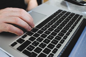 Stock Image: Closeup male hands typing on notebook keyboard at home office. Man using laptop