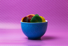 Stock Image: colorful sugar snails (wine gum) in a bowl on a pink and white striped background