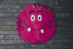 Stock Image: Friendly smiling pink monster on wooden background