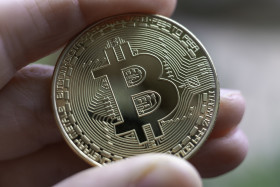 Stock Image: Golden Bitcoin between human fingers