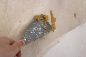 Stock Image: Hands removing old wallpaper with the help of a spatula during the repair in the room.