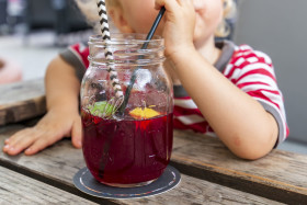 Stock Image: Little Child drink juice or ice tea or summer drink from glasses through straws