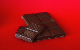 Stock Image: Pieces of dark chocolate isolated on red background.