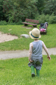 Stock Image: Toddler in rubber boots and with a hat on his head walks across a meadow