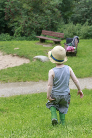 Stock Image: Toddler in rubber boots and with a hat on his head walks across a meadow