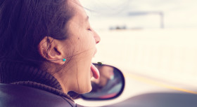 Stock Image: woman looks out of a window from a moving car and sticks out her tongue